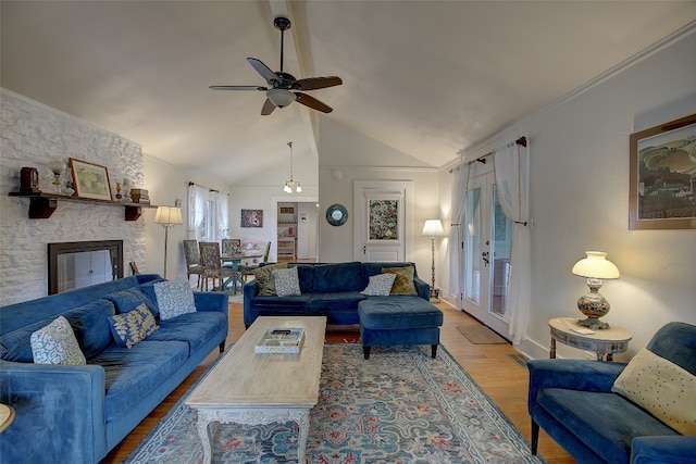 living room with a stone fireplace, ceiling fan, lofted ceiling, wood-type flooring, and ornamental molding