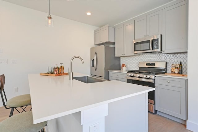 kitchen featuring a breakfast bar area, tasteful backsplash, light wood-style flooring, appliances with stainless steel finishes, and a sink