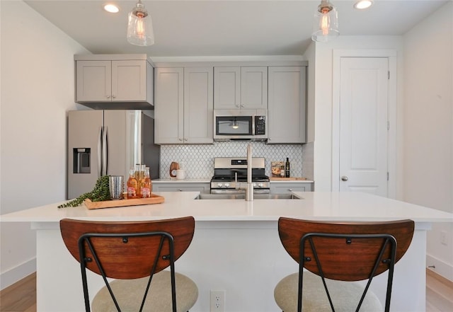 kitchen featuring stainless steel appliances, a kitchen bar, gray cabinets, and decorative backsplash