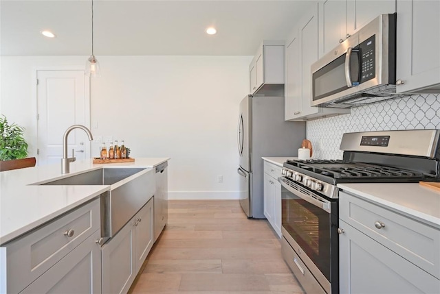 kitchen featuring light wood-style floors, appliances with stainless steel finishes, light countertops, and backsplash