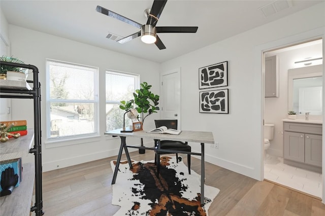 home office with light wood-style floors, visible vents, and a sink