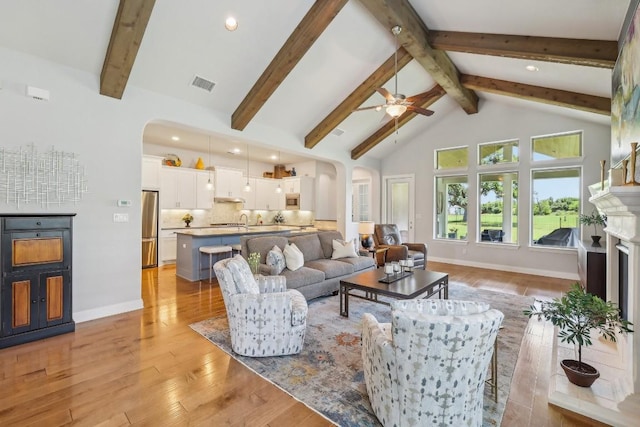 living room featuring light wood-type flooring, ceiling fan, sink, high vaulted ceiling, and beamed ceiling