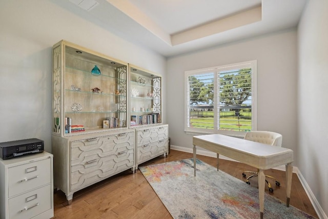 office area with light hardwood / wood-style floors and a tray ceiling