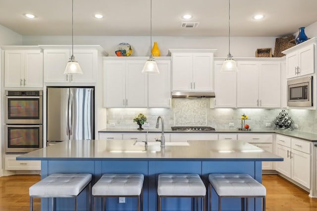 kitchen with stainless steel appliances, hanging light fixtures, light hardwood / wood-style floors, a kitchen bar, and a kitchen island with sink