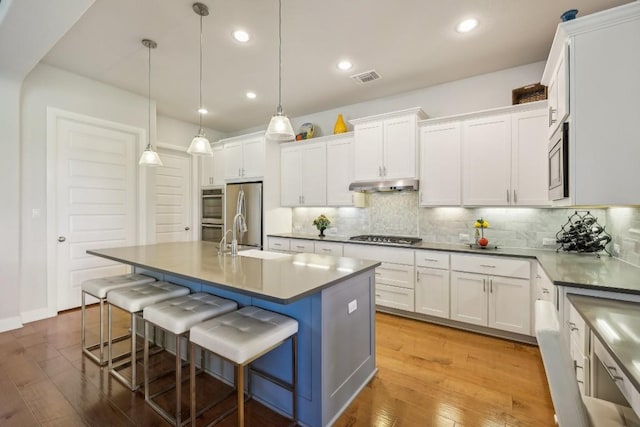 kitchen with white cabinetry, sink, a kitchen breakfast bar, pendant lighting, and light hardwood / wood-style floors