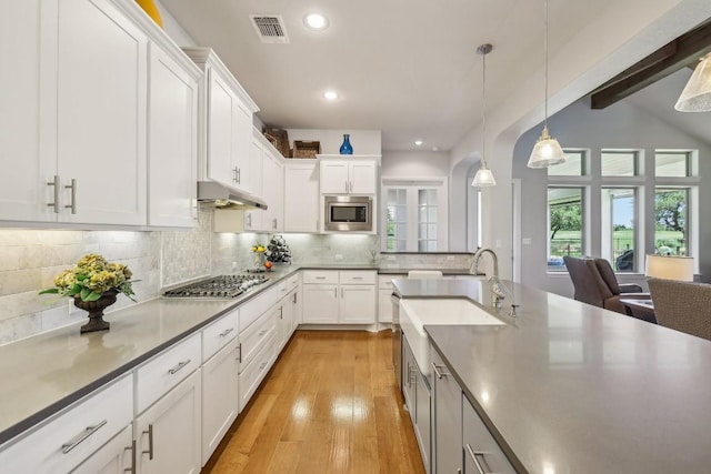 kitchen featuring stainless steel appliances, light hardwood / wood-style floors, decorative light fixtures, decorative backsplash, and white cabinets