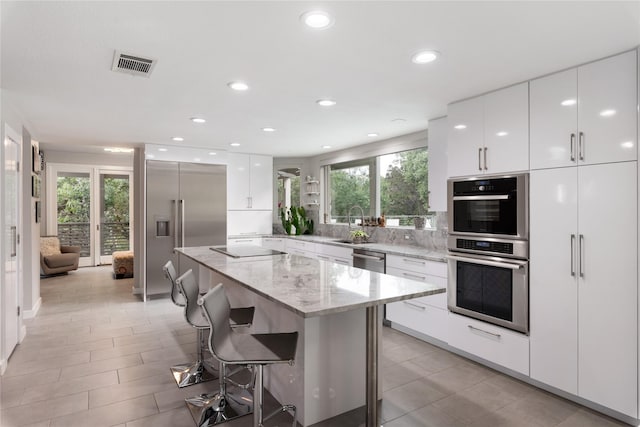 kitchen featuring white cabinetry, appliances with stainless steel finishes, a center island, and a kitchen bar