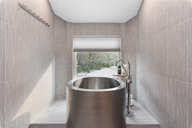 bathroom with tile patterned flooring, a bathing tub, and tile walls