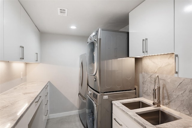 clothes washing area featuring sink, cabinets, and stacked washer / dryer