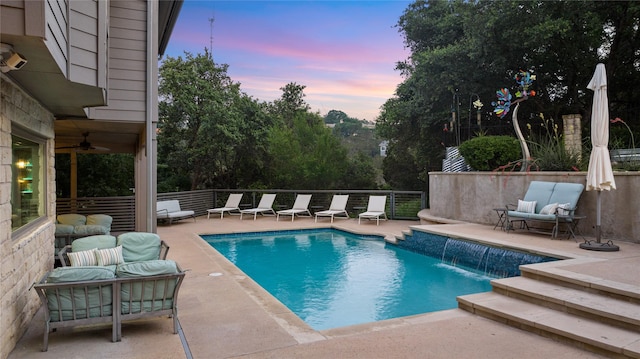 pool at dusk featuring ceiling fan, outdoor lounge area, pool water feature, and a patio area