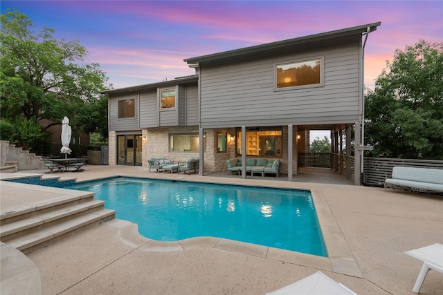 pool at dusk with an outdoor living space and a patio