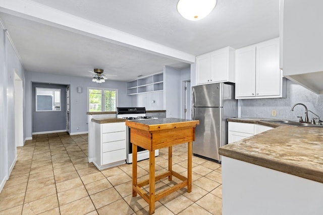 kitchen featuring sink, stainless steel refrigerator, ceiling fan, white cabinetry, and gas range