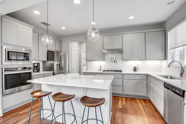 kitchen featuring stainless steel appliances, sink, light hardwood / wood-style floors, a kitchen island, and pendant lighting