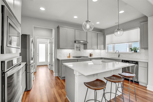 kitchen with pendant lighting, a kitchen island, gray cabinets, appliances with stainless steel finishes, and sink