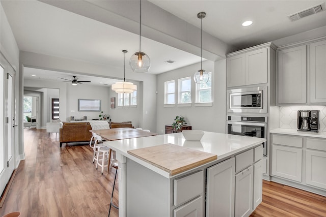 kitchen featuring stainless steel appliances, ceiling fan, backsplash, hanging light fixtures, and a kitchen island