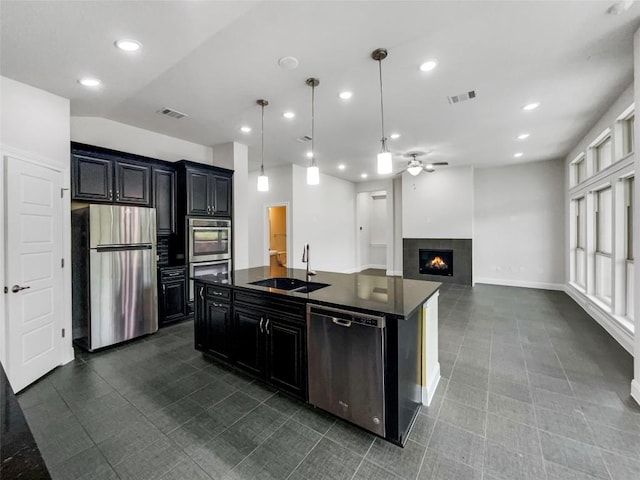 kitchen with sink, a fireplace, appliances with stainless steel finishes, an island with sink, and decorative light fixtures