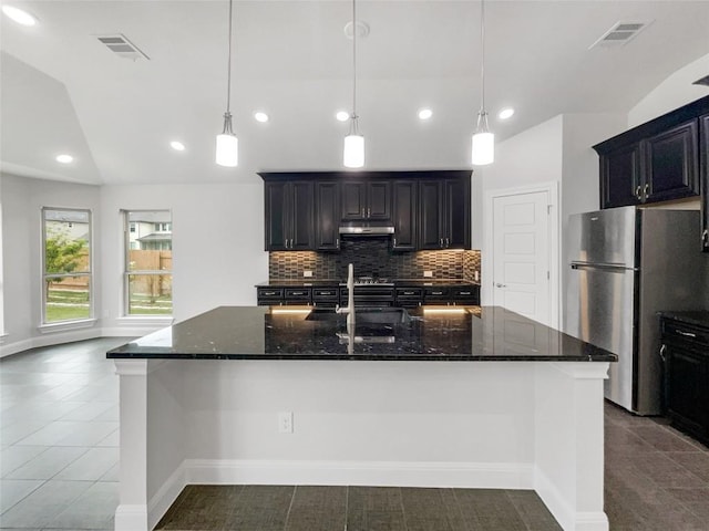 kitchen with lofted ceiling, a large island with sink, sink, stainless steel fridge, and dark stone countertops