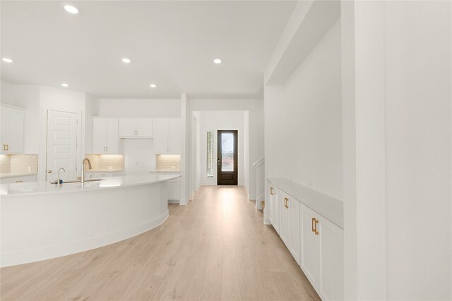 kitchen with white cabinetry, tasteful backsplash, sink, and light wood-type flooring