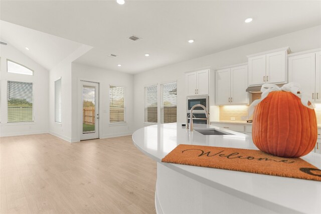 kitchen featuring vaulted ceiling, white cabinets, light hardwood / wood-style floors, and tasteful backsplash