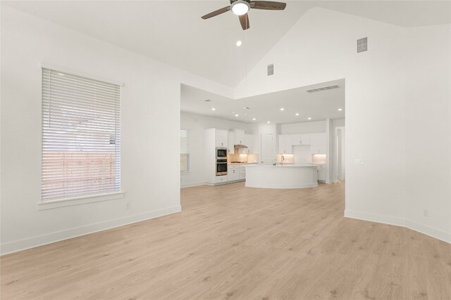 unfurnished living room featuring ceiling fan, high vaulted ceiling, sink, and light wood-type flooring