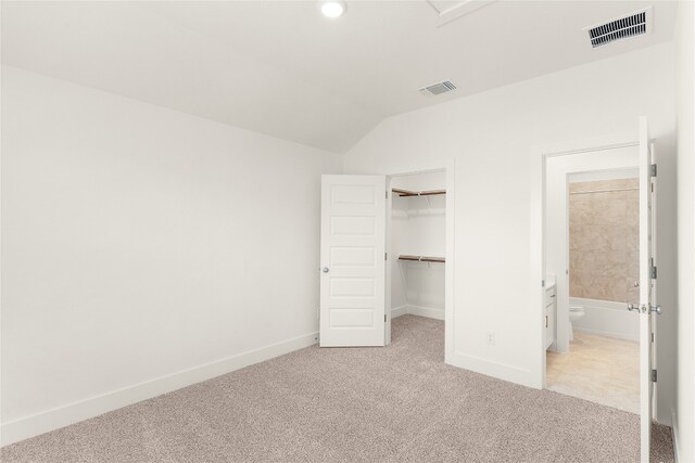 unfurnished bedroom featuring a closet, lofted ceiling, a spacious closet, and light colored carpet