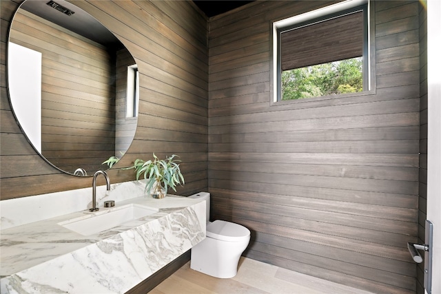 bathroom featuring toilet, sink, and wooden walls