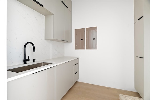 kitchen with light wood-type flooring, electric panel, tasteful backsplash, and sink