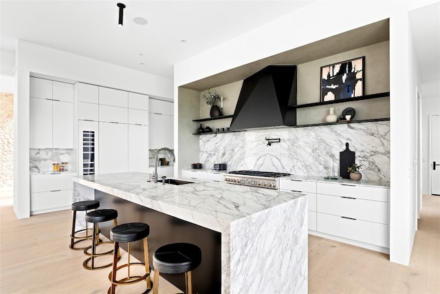 kitchen with decorative backsplash, ventilation hood, a kitchen island with sink, sink, and a breakfast bar area