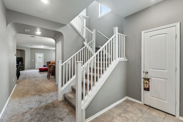 tiled foyer with stairway, baseboards, arched walkways, and carpet flooring