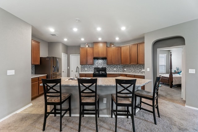 kitchen with arched walkways, black range with electric cooktop, a sink, a kitchen breakfast bar, and stainless steel fridge with ice dispenser