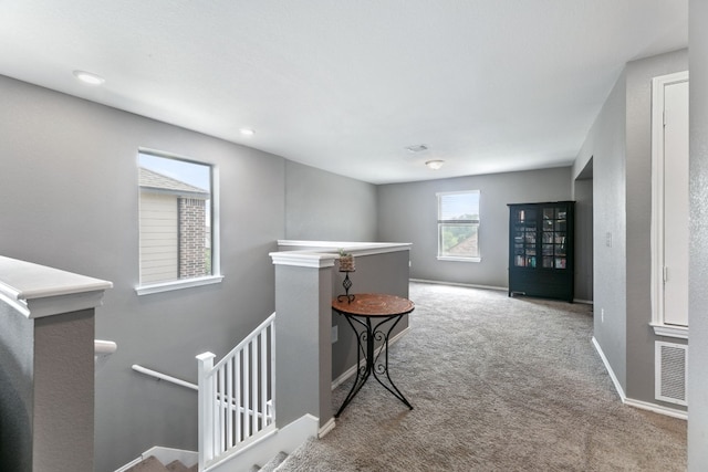 hallway with carpet floors, visible vents, baseboards, and an upstairs landing