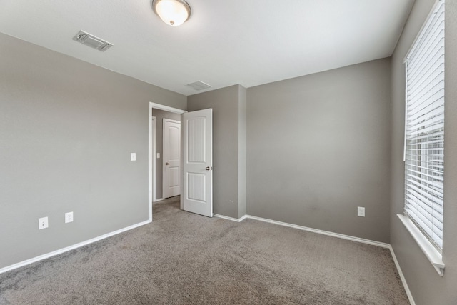 empty room with carpet, visible vents, and baseboards