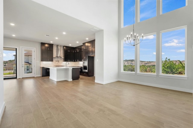 kitchen featuring double oven, open floor plan, plenty of natural light, and wall chimney range hood