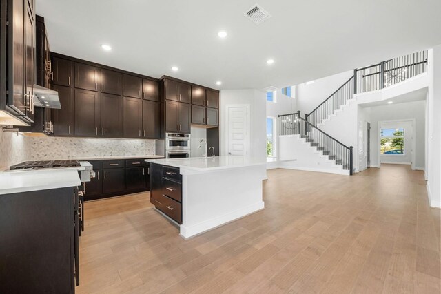 kitchen featuring light hardwood / wood-style floors, wall chimney range hood, a kitchen island with sink, and dark brown cabinets