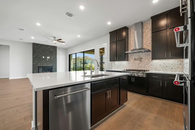 kitchen with a large fireplace, appliances with stainless steel finishes, light hardwood / wood-style floors, ceiling fan, and wall chimney range hood