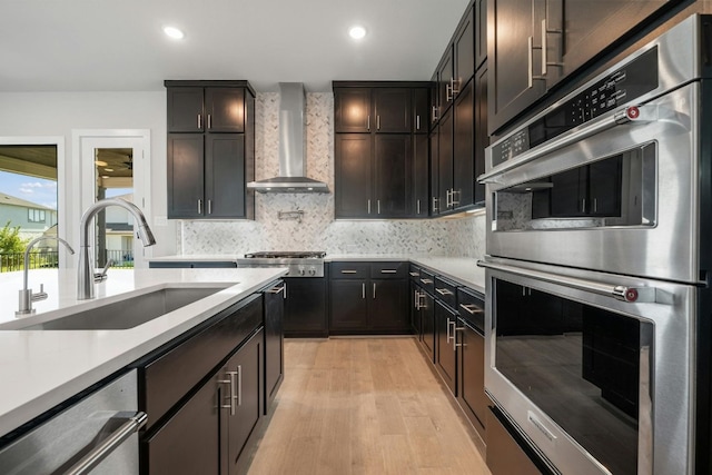 kitchen featuring decorative backsplash, wall chimney exhaust hood, appliances with stainless steel finishes, light countertops, and a sink