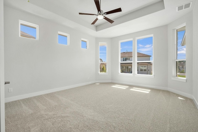 carpeted empty room with ceiling fan, baseboards, visible vents, and a raised ceiling