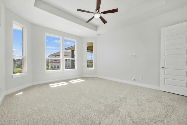 carpeted spare room featuring a tray ceiling, a ceiling fan, and baseboards