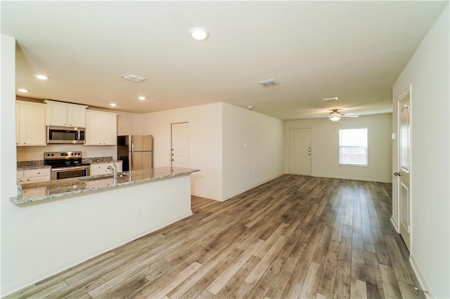 kitchen featuring light stone countertops, sink, light hardwood / wood-style flooring, white cabinets, and appliances with stainless steel finishes