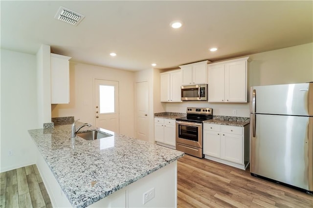 kitchen featuring kitchen peninsula, appliances with stainless steel finishes, light wood-type flooring, sink, and white cabinetry