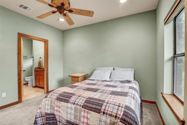 bedroom featuring ceiling fan, light colored carpet, and ensuite bath