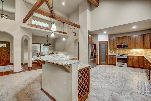 kitchen featuring appliances with stainless steel finishes, backsplash, a towering ceiling, a kitchen breakfast bar, and decorative light fixtures