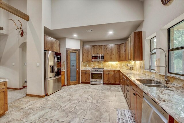 kitchen with appliances with stainless steel finishes, sink, decorative backsplash, a high ceiling, and light stone counters