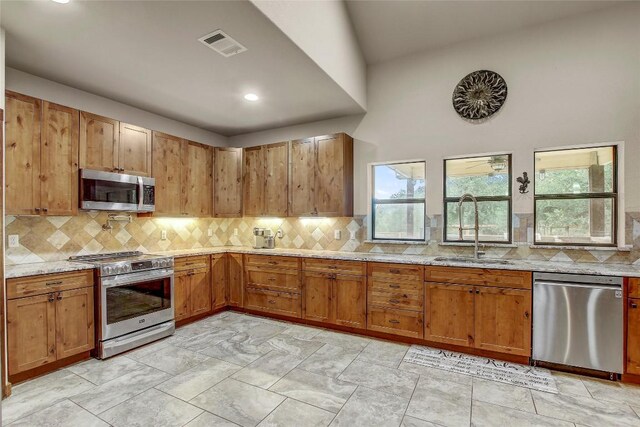 kitchen with light stone countertops, appliances with stainless steel finishes, sink, and a healthy amount of sunlight