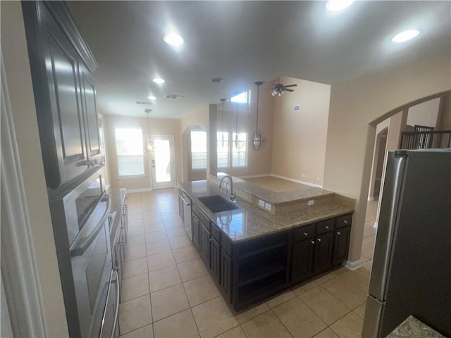 kitchen with sink, ceiling fan, light stone countertops, light tile patterned flooring, and stainless steel appliances