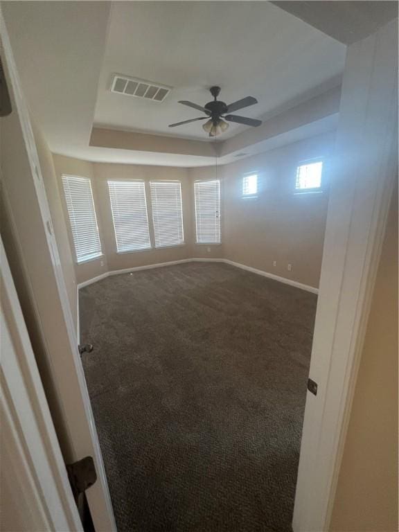 carpeted spare room with a raised ceiling and ceiling fan