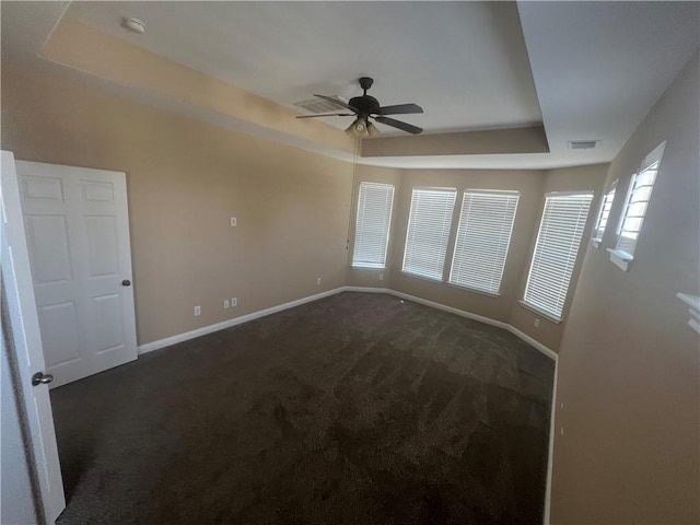 unfurnished room featuring a tray ceiling, ceiling fan, and dark colored carpet