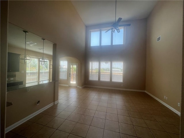 unfurnished room featuring tile patterned flooring, a towering ceiling, and ceiling fan with notable chandelier