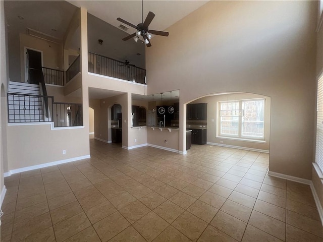 unfurnished living room with ceiling fan, a towering ceiling, and light tile patterned floors