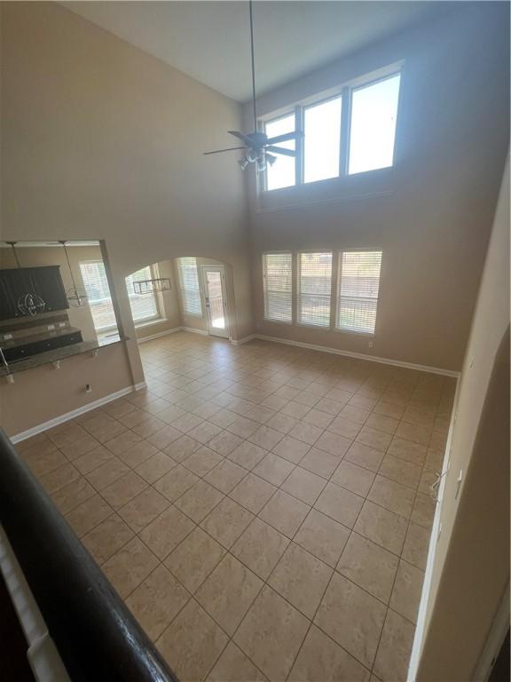 unfurnished living room with a wealth of natural light, a high ceiling, light tile patterned floors, and ceiling fan